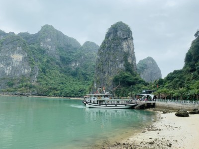 A view of the sandy bay when you pull up to see Sung Sot cave as part of your 1 day Halong Bay tour.  You can see lots of limestone rocks here and a cruise boat moored in the bay.