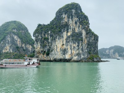 A view of part of Halong Bay that you can see on a on a Halong Bay day cruise.  You see the limestone islands and a boat sailing between them.