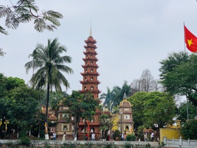 The Tran Quoc Pagoda, a must on 4 days in Hanoi.  You can see the long tall pagoda here with its different platforms going through it.  You can also see palm trees and the Vietnamese flag on the right.  It is flanked by smaller temples.