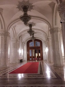 A walkway in the Palace that you can see when visiting this Bucharest attraction.  This is white and marble and with a red carpet on the floor and chandeliers hanging from the ceiling