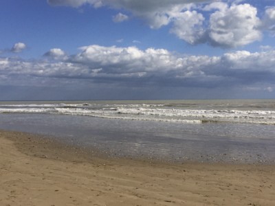 Rimini beach with the gentle waves lapping the sand and clouds in the blue sky