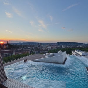 The rooftop pool of the spa.  You can see two people in the pool and there are views out across Zurich city