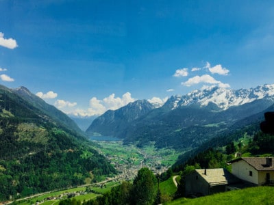 A view from the Bernina Express train.  You can see a few small houses in the front on the green hills, a valley with the lake at bottom and snow capped mountains surrounding the valley