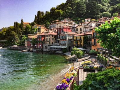 The view of Varenna, one of the small towns on Lake Como. You can see a small bay, the colourful houses, the trees behind and some canoes on the shoreline.