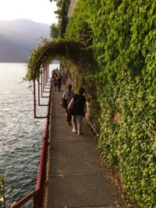 The walkway in Varenna around the side of the lake. It is covered in vegetation with a red railing