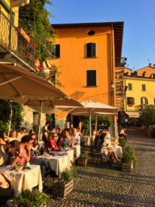 An image of some of the cafes and bars by the lake in Varenna. You can see tables with parasols and people sitting outside