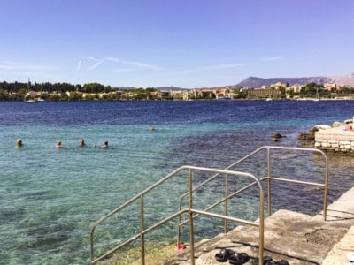 A lido on the outskirts of Corfu Town.  There are steps leading into the sea and people swimming in the sea