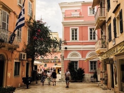 A square in the old town in Corfu Town.  It's surrounded by a pink pastel and orange pastel buildings.