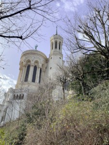 The Basilique Notre Dame de Fourvière from the pathway leading back to the old part of Lyon. You can see trees and bushes in the foreground.