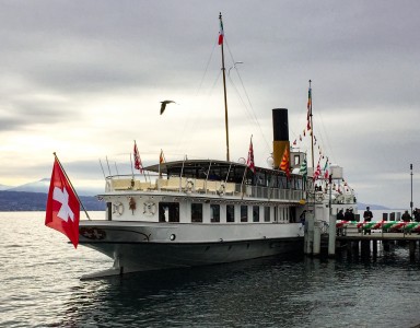 A ferry boat on the lake at Ouchy in Lausanne.  It has the Swiss flag flying from the front.
